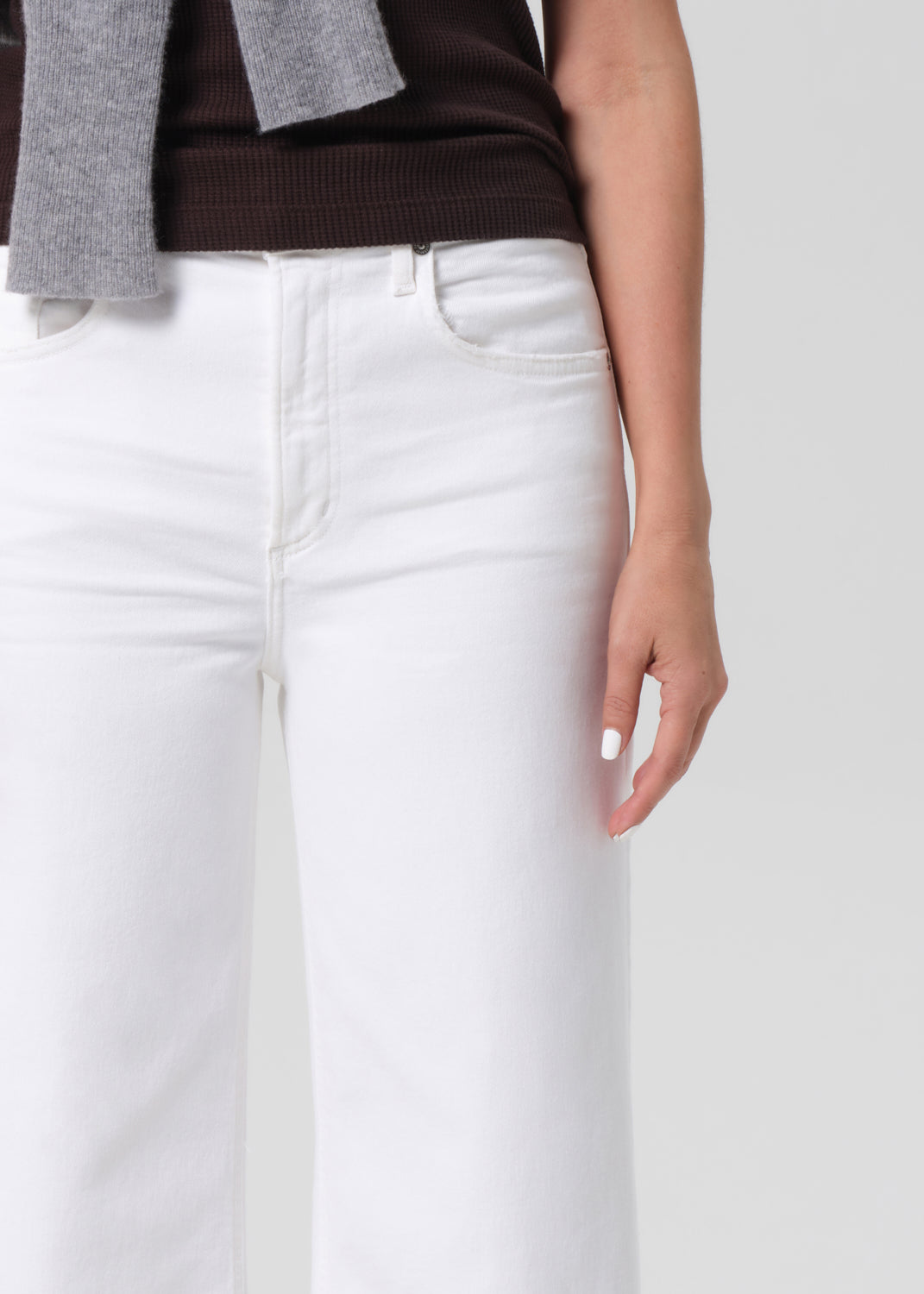 Person wearing a brown sleeveless top, white pants on a light gray background