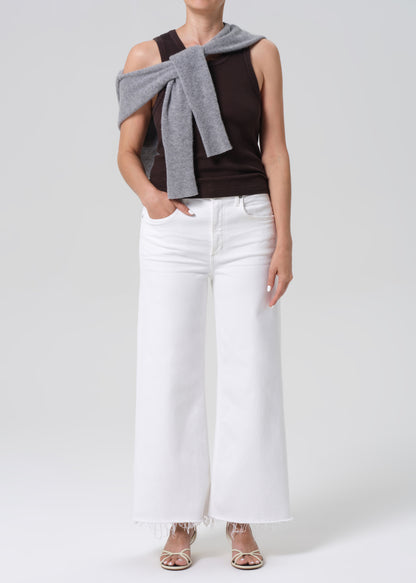 Person wearing a brown sleeveless top, white pants on a light gray background