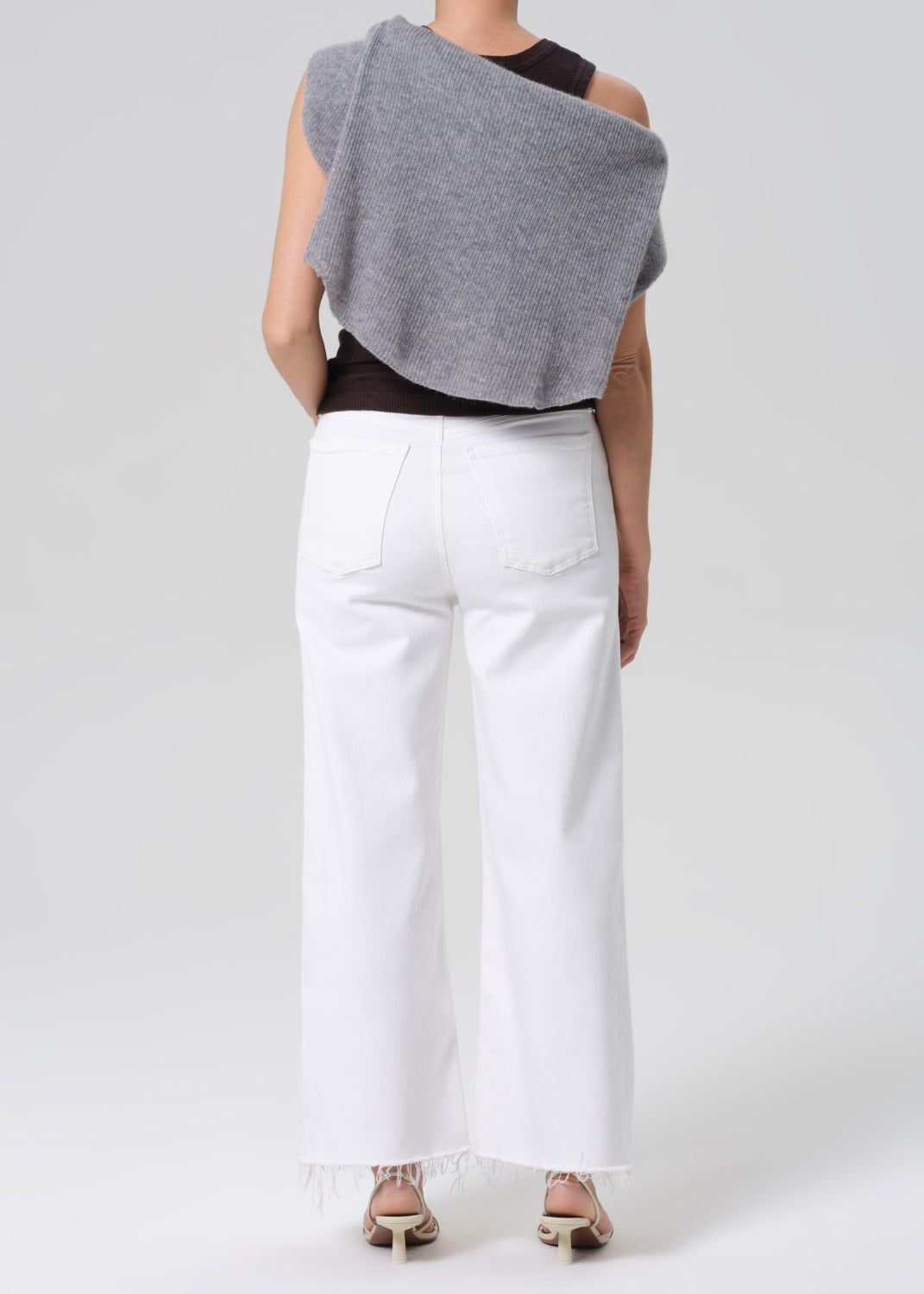 Person wearing a brown sleeveless top, white pants on a light gray background