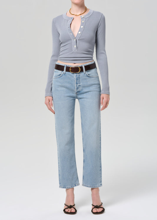 Person wearing a gray long-sleeve top and light blue jeans on a grey background