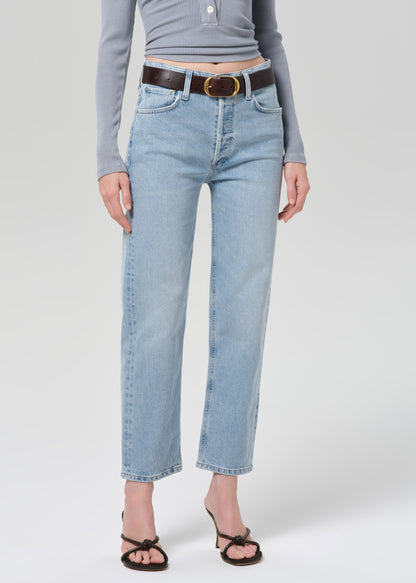 Person wearing a gray long-sleeve top and light blue jeans on a grey background