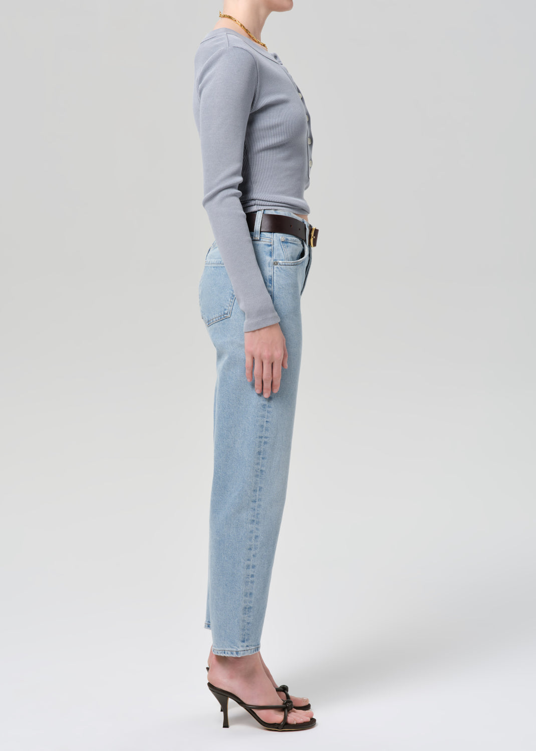 Person wearing a gray long-sleeve top and light blue jeans on a grey background