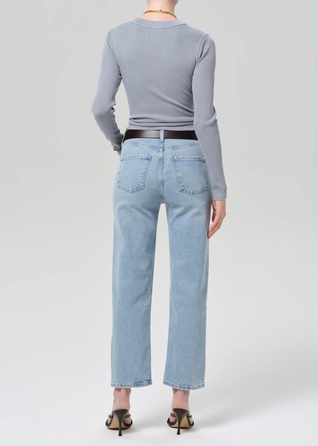 Person wearing a gray long-sleeve top and light blue jeans on a grey background