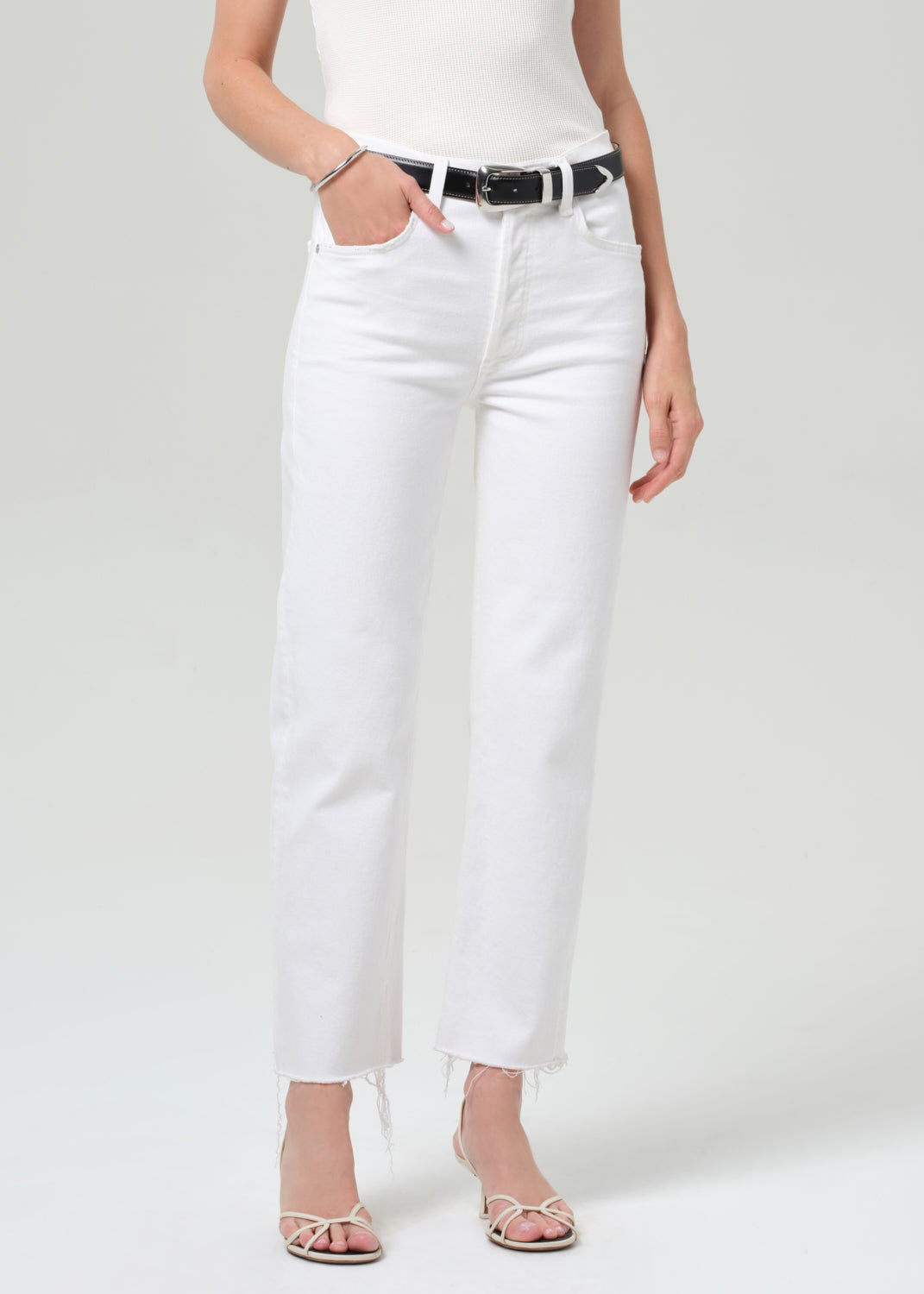 Person wearing white jeans with a black belt on a light gray background
