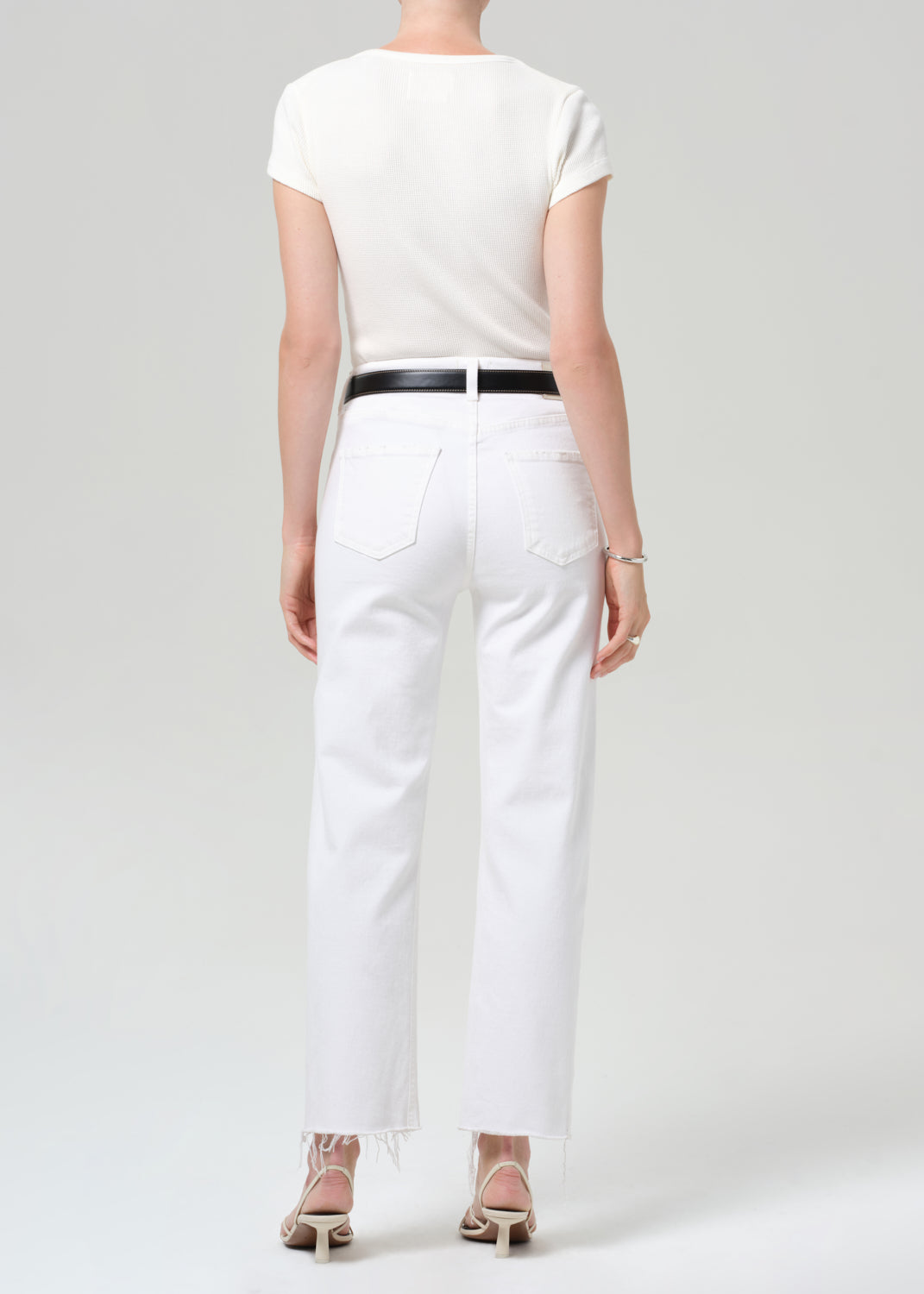 Person wearing a white top and white pants with a black belt on a light gray background