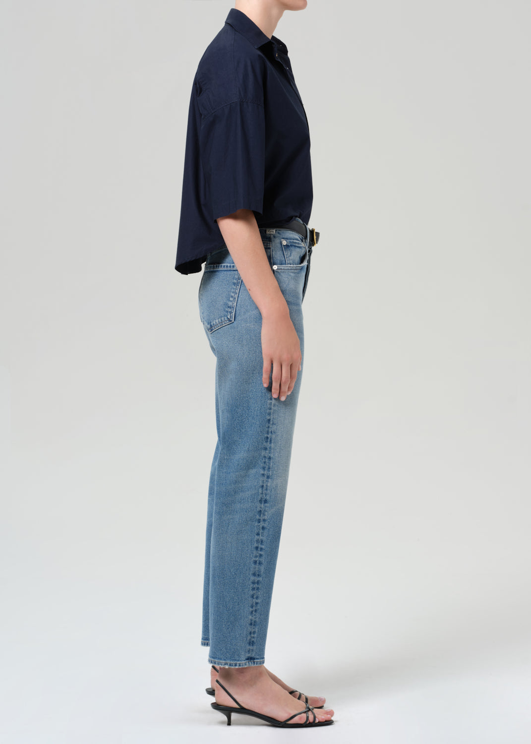 Person wearing a navy shirt and light blue jeans on a grey background