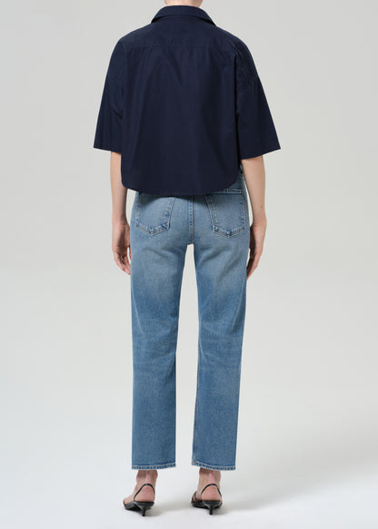 Person wearing a navy shirt and light blue jeans on a grey background