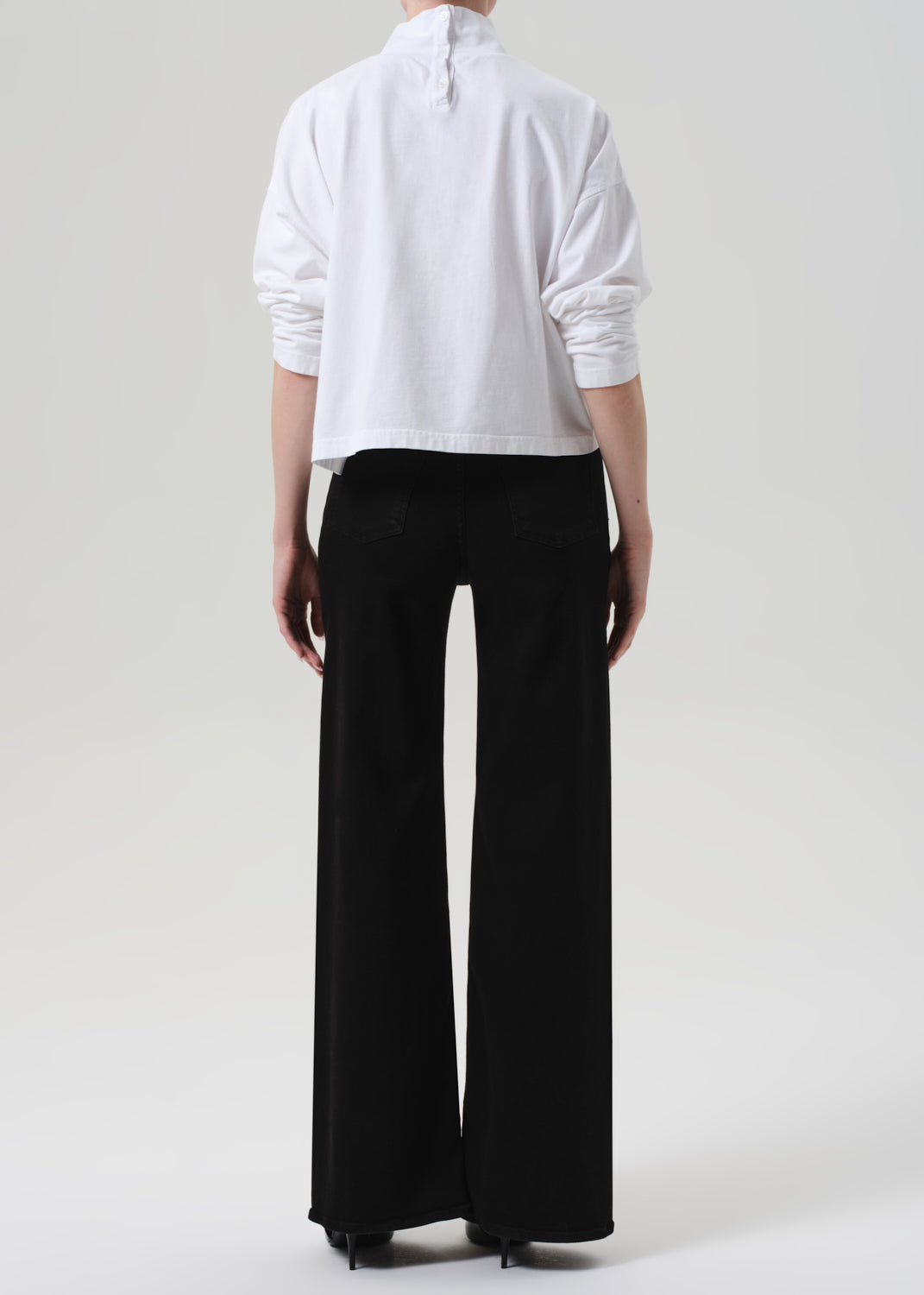 Person wearing a white shirt and black jeans on a plain background