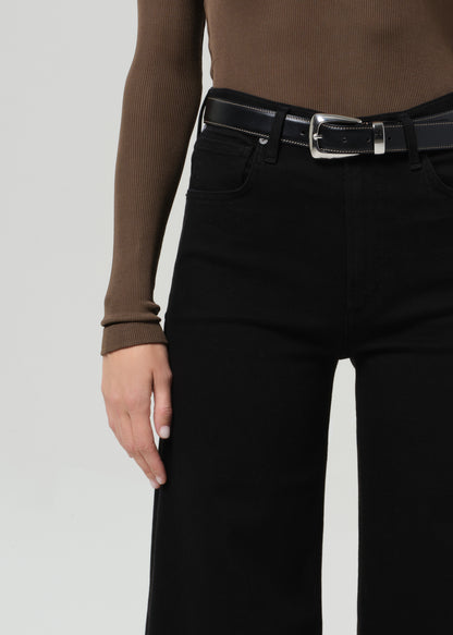 Person wearing a brown long-sleeve shirt and black wide-leg jean on a plain background