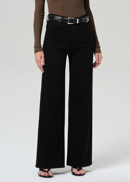 Person wearing a brown long-sleeve shirt and black wide-leg jean on a plain background