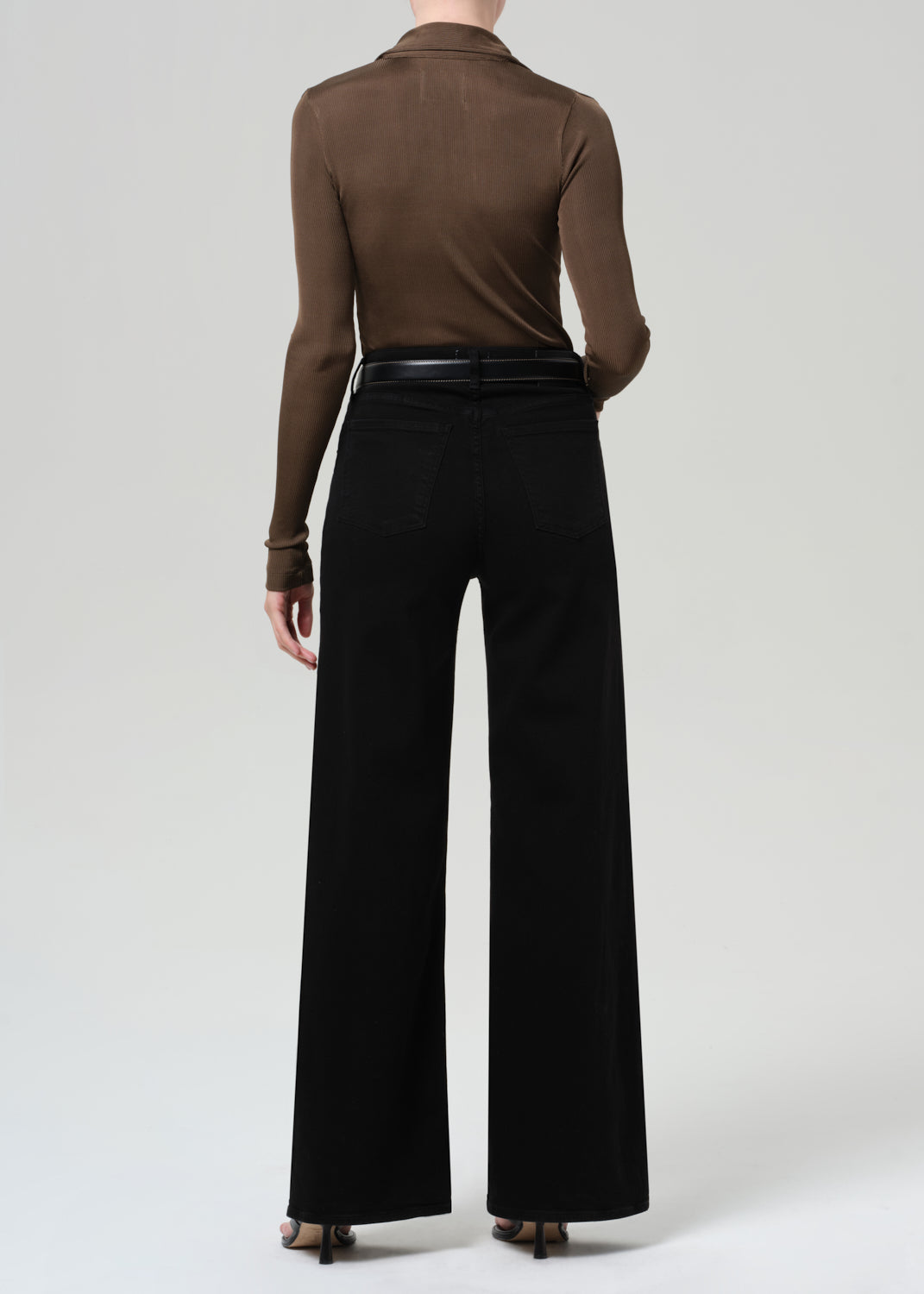 Person wearing a brown long-sleeve shirt and black wide-leg jean on a plain background