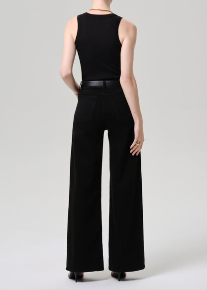 A model shown from the back wearing a black sleeveless top and black wide-leg trousers with a thin black belt, photographed against a grey background.