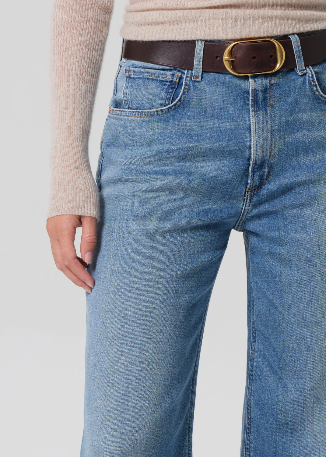 Person wearing a beige sweater and blue jeans on a grey background