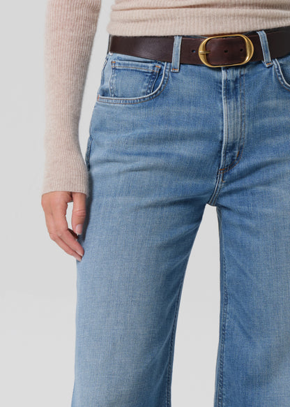 Person wearing a beige sweater and blue jeans on a grey background