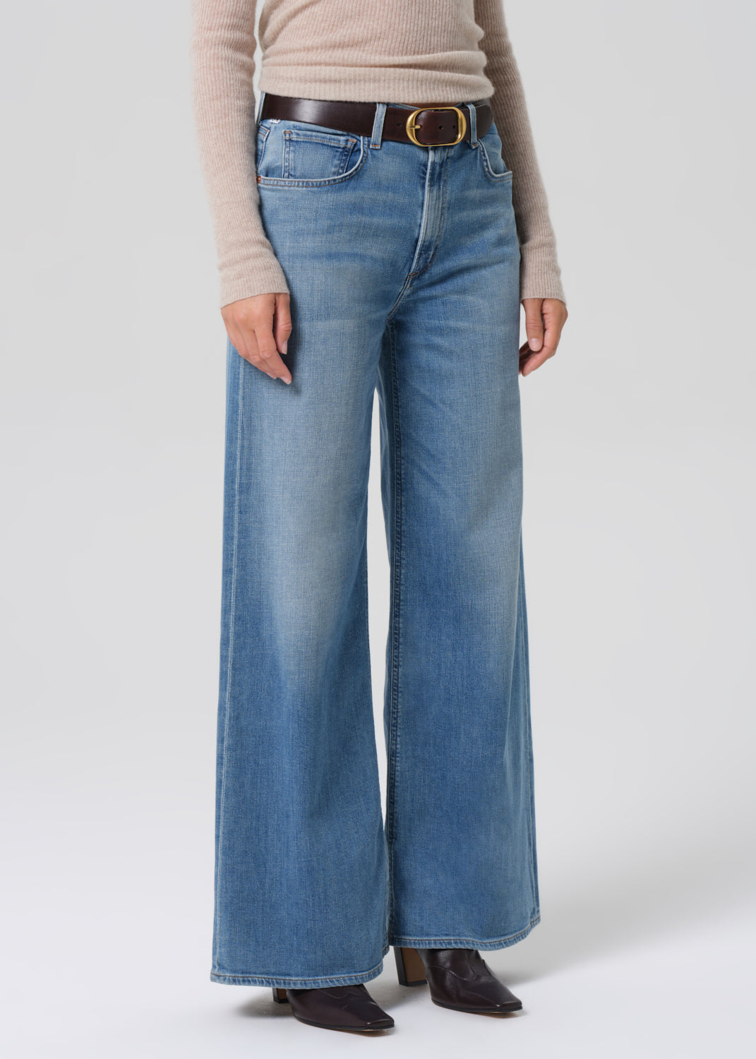 Person wearing a beige sweater and blue jeans on a grey background