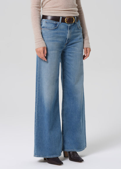 Person wearing a beige sweater and blue jeans on a grey background