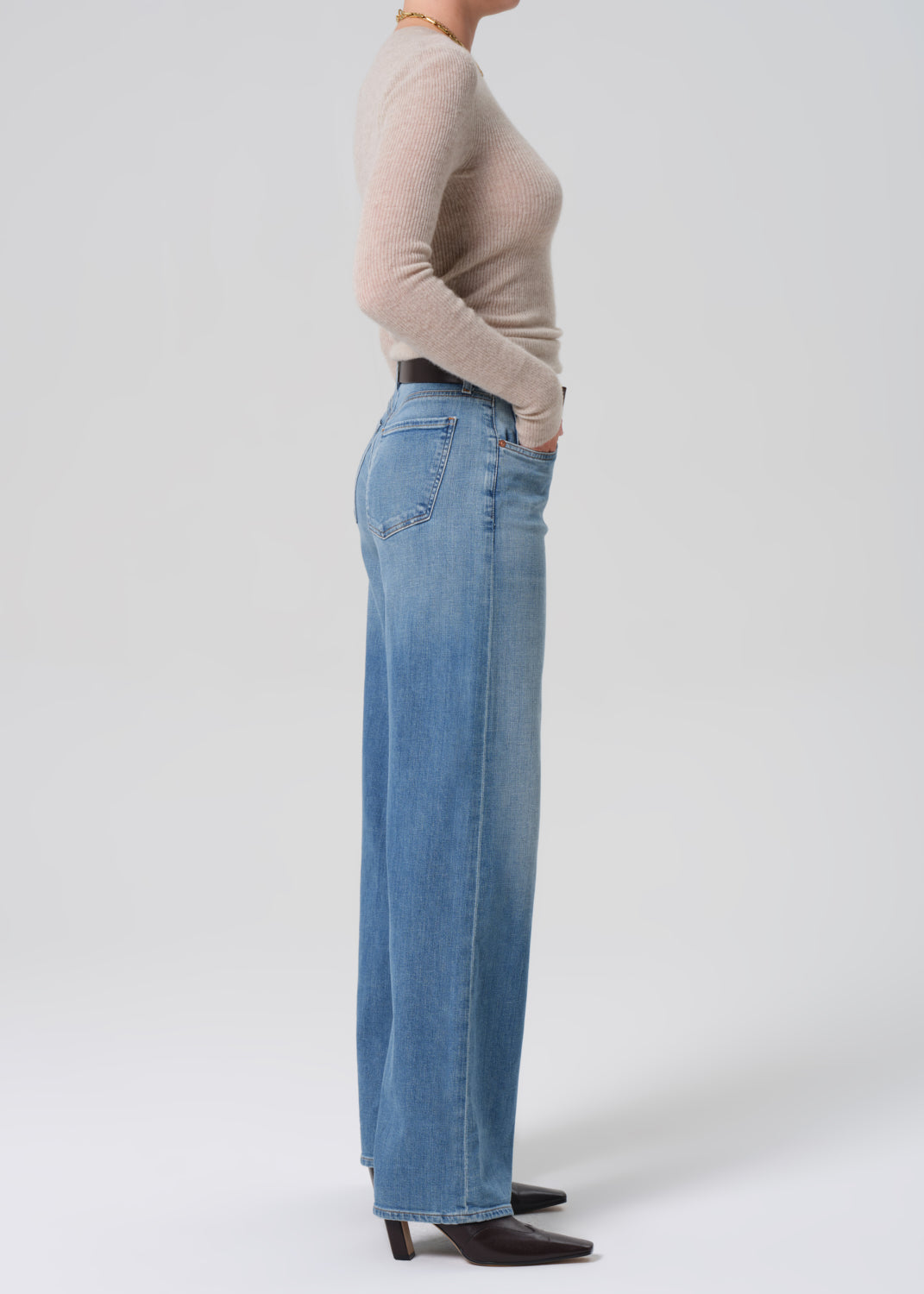 Person wearing a beige sweater and blue jeans on a grey background