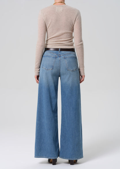 Person wearing a beige sweater and blue jeans on a grey background