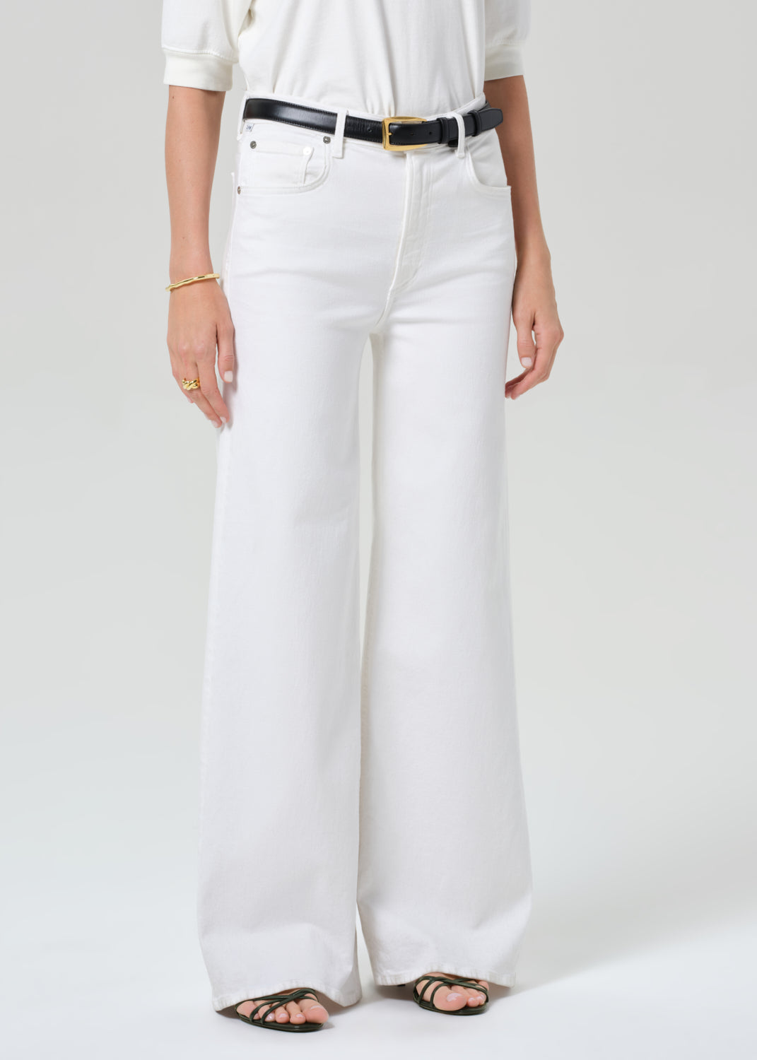 Person wearing white jeans with a black belt on a plain background