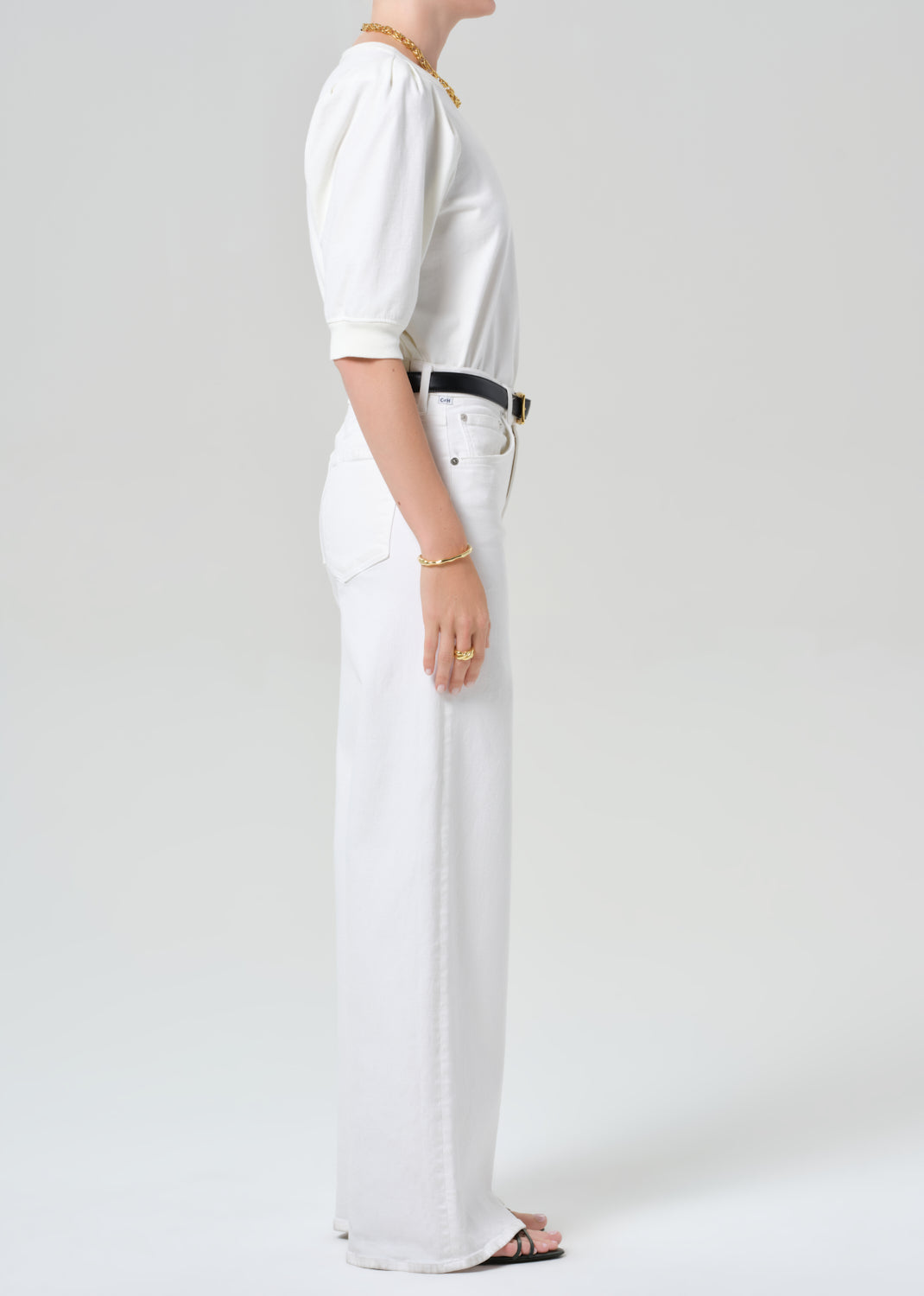 Person wearing a white outfit with a belt on a plain background