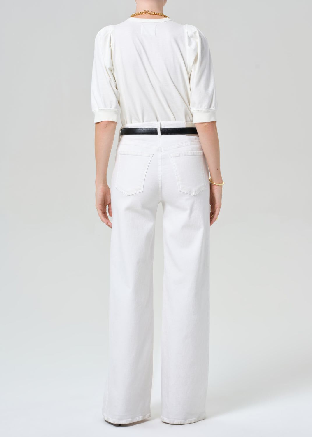 Person wearing a white outfit with a black belt on a plain background