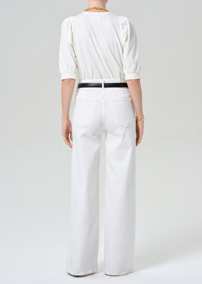 Person wearing a white outfit with a black belt on a plain background