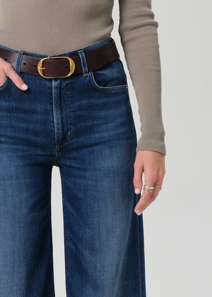 Person wearing a beige long-sleeve top and blue jeans on a grey background