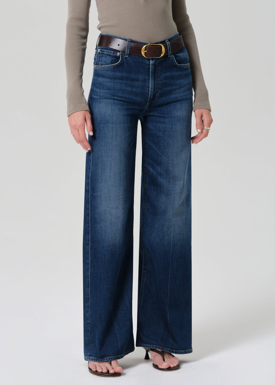 Person wearing a beige long-sleeve top and blue jeans on a grey background