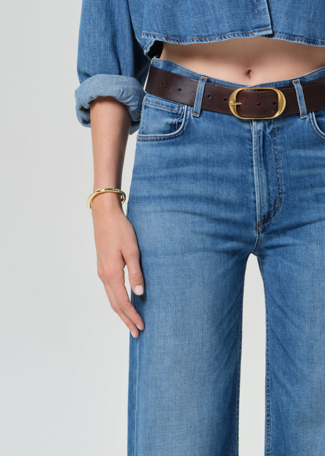 Person wearing a blue denim cropped shirt and jeans with a grey background