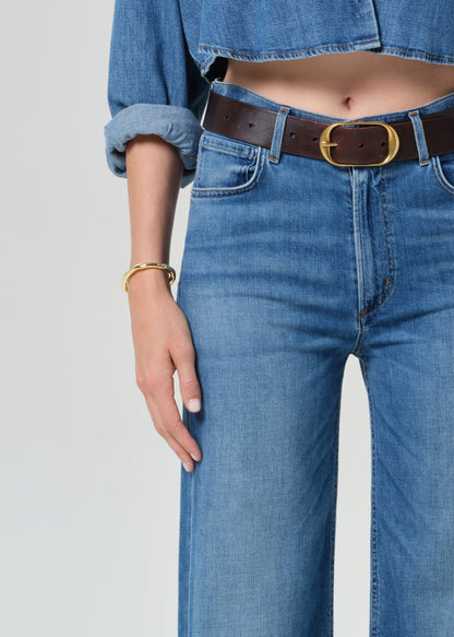 Person wearing a blue denim cropped shirt and jeans with a grey background