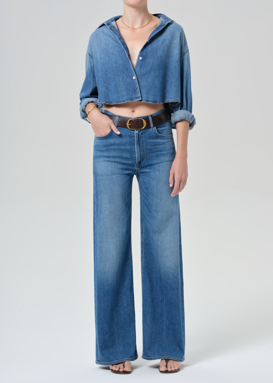 Person wearing a blue denim cropped shirt and jeans with a grey background