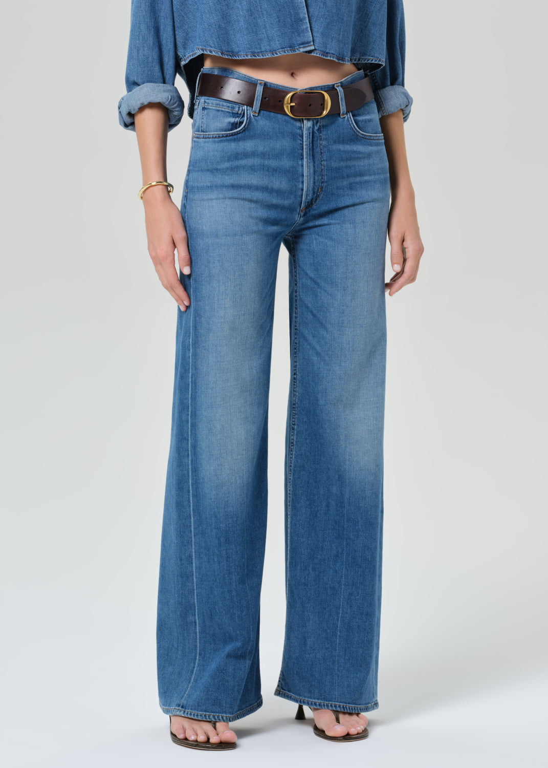 Person wearing a blue denim cropped shirt and jeans with a grey background