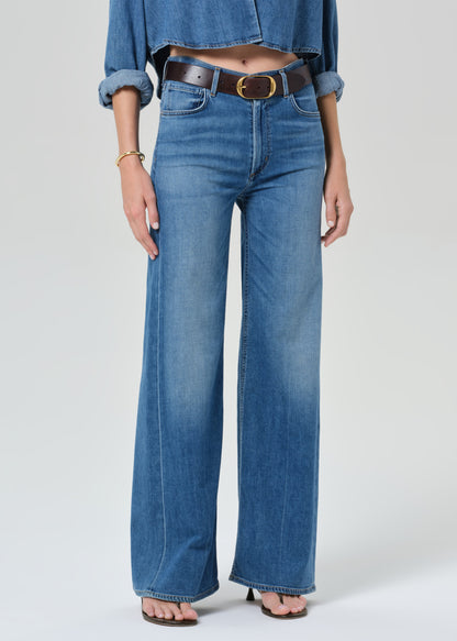 Person wearing a blue denim cropped shirt and jeans with a grey background