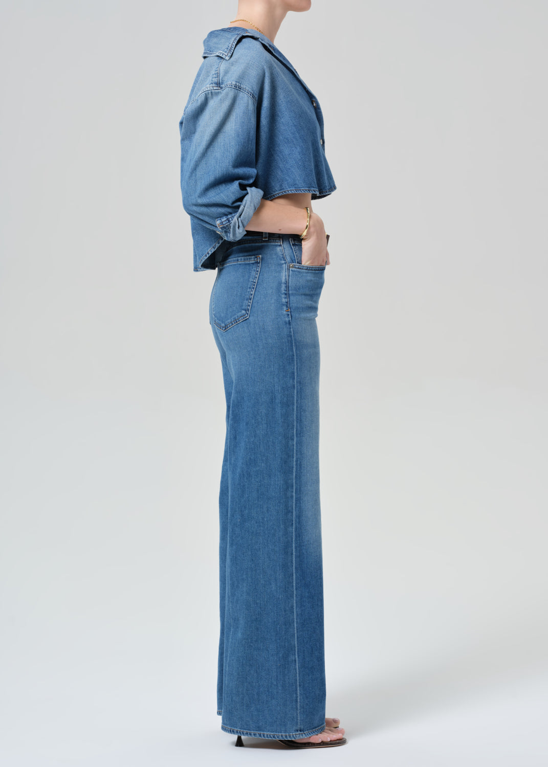 Person wearing a blue denim cropped shirt and jeans with a grey background