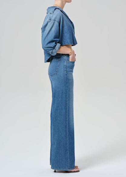 Person wearing a blue denim cropped shirt and jeans with a grey background