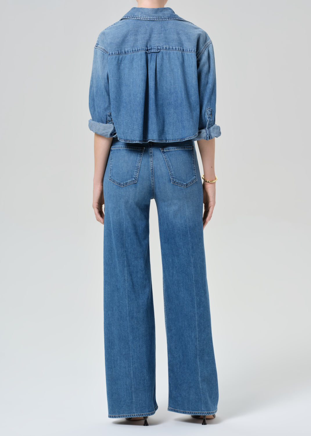 Person wearing a blue denim cropped shirt and jeans with a grey background