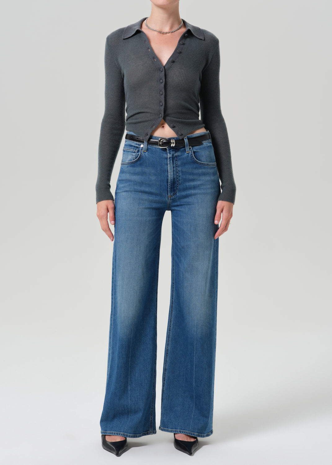 Person wearing grey cardigan sweater with blue jeans on a grey background