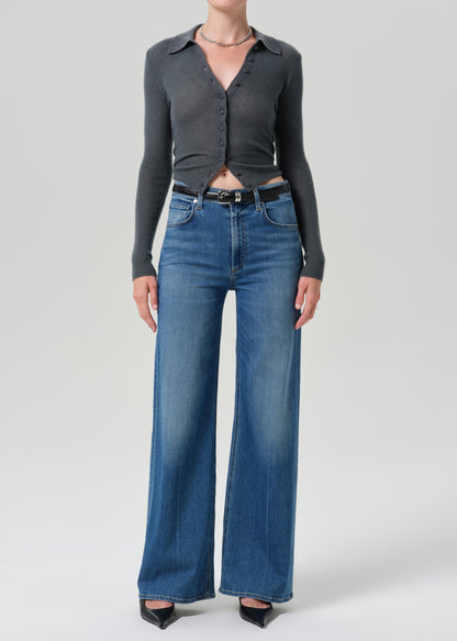 Person wearing grey cardigan sweater with blue jeans on a grey background