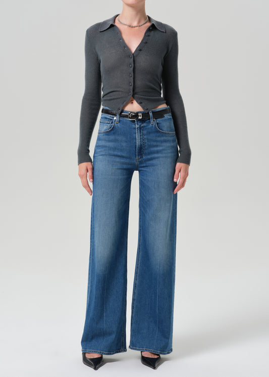Person wearing grey cardigan sweater with blue jeans on a grey background