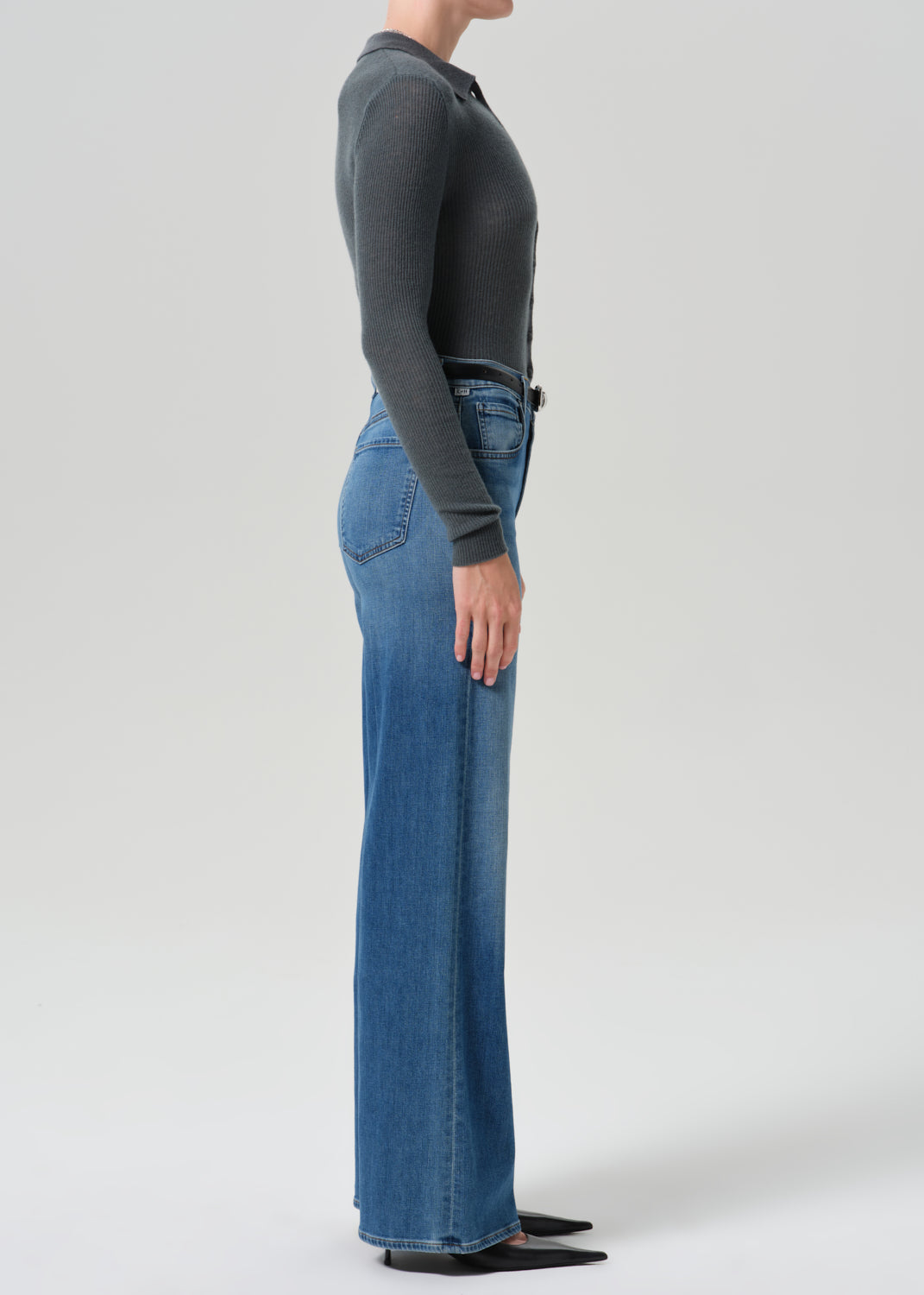 Person wearing grey cardigan sweater with blue jeans on a grey background