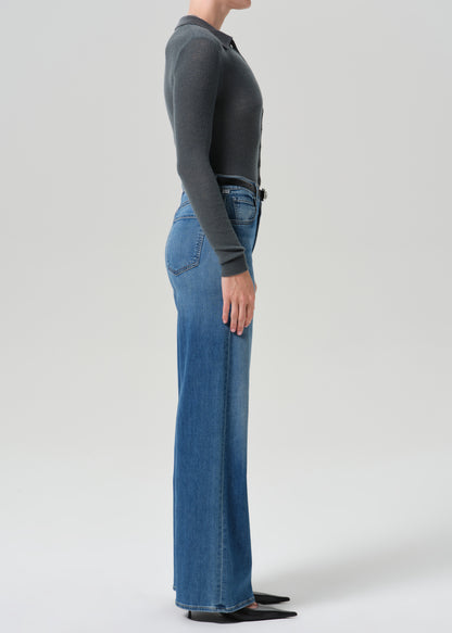 Person wearing grey cardigan sweater with blue jeans on a grey background