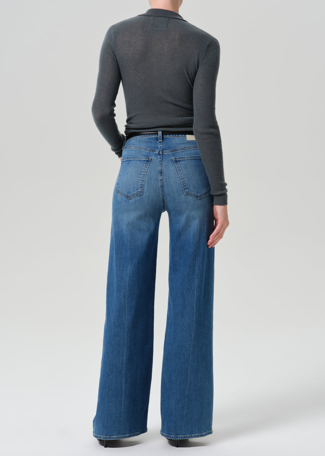 Person wearing grey cardigan sweater with blue jeans on a grey background