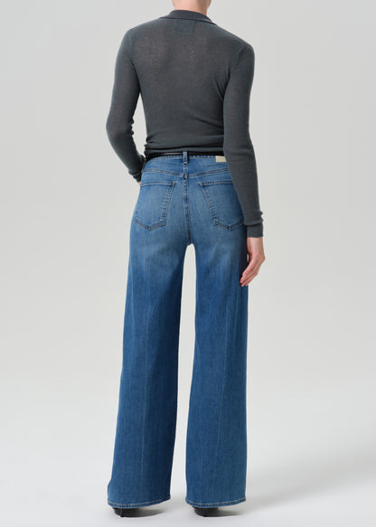 Person wearing grey cardigan sweater with blue jeans on a grey background