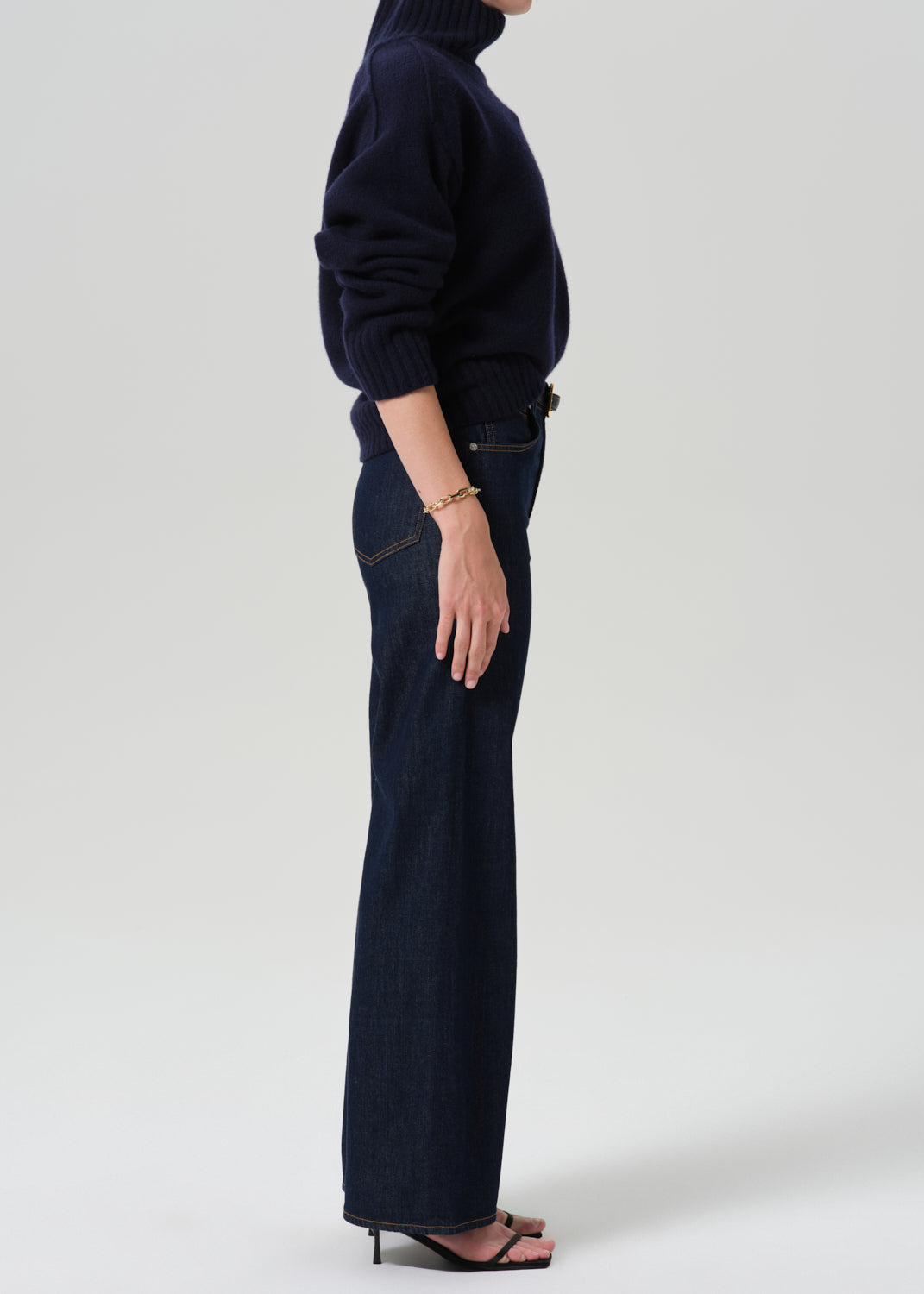 Person wearing a blue turtleneck with dark blue pants on a grey background