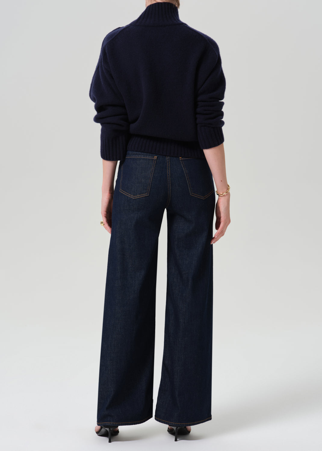 Person wearing a blue turtleneck with dark blue pants on a grey background