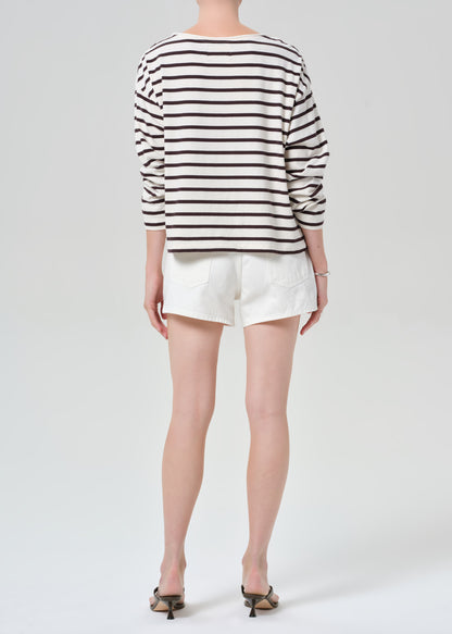 Person wearing a brown and white striped sweater with white shorts on a plain background