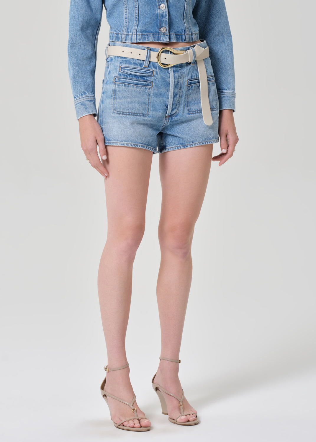 Person wearing a denim jacket and shorts on a grey background