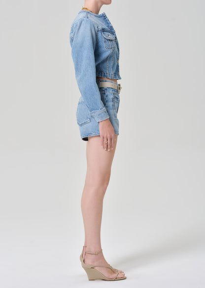 Person wearing a denim jacket and shorts on a grey background