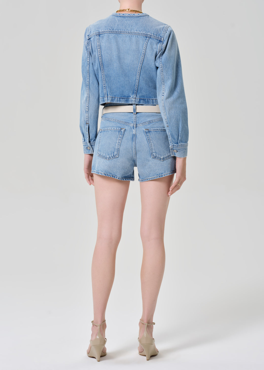 Person wearing a denim jacket and shorts on a grey background