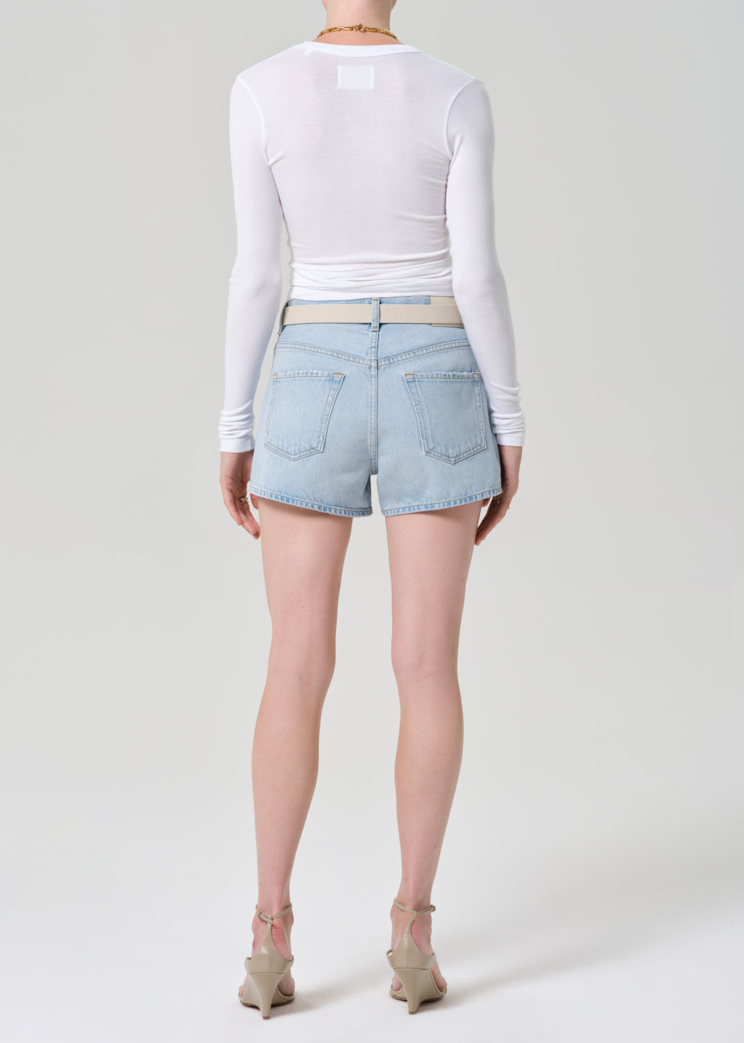 Person wearing light blue denim shorts and a white long-sleeve top on a plain background